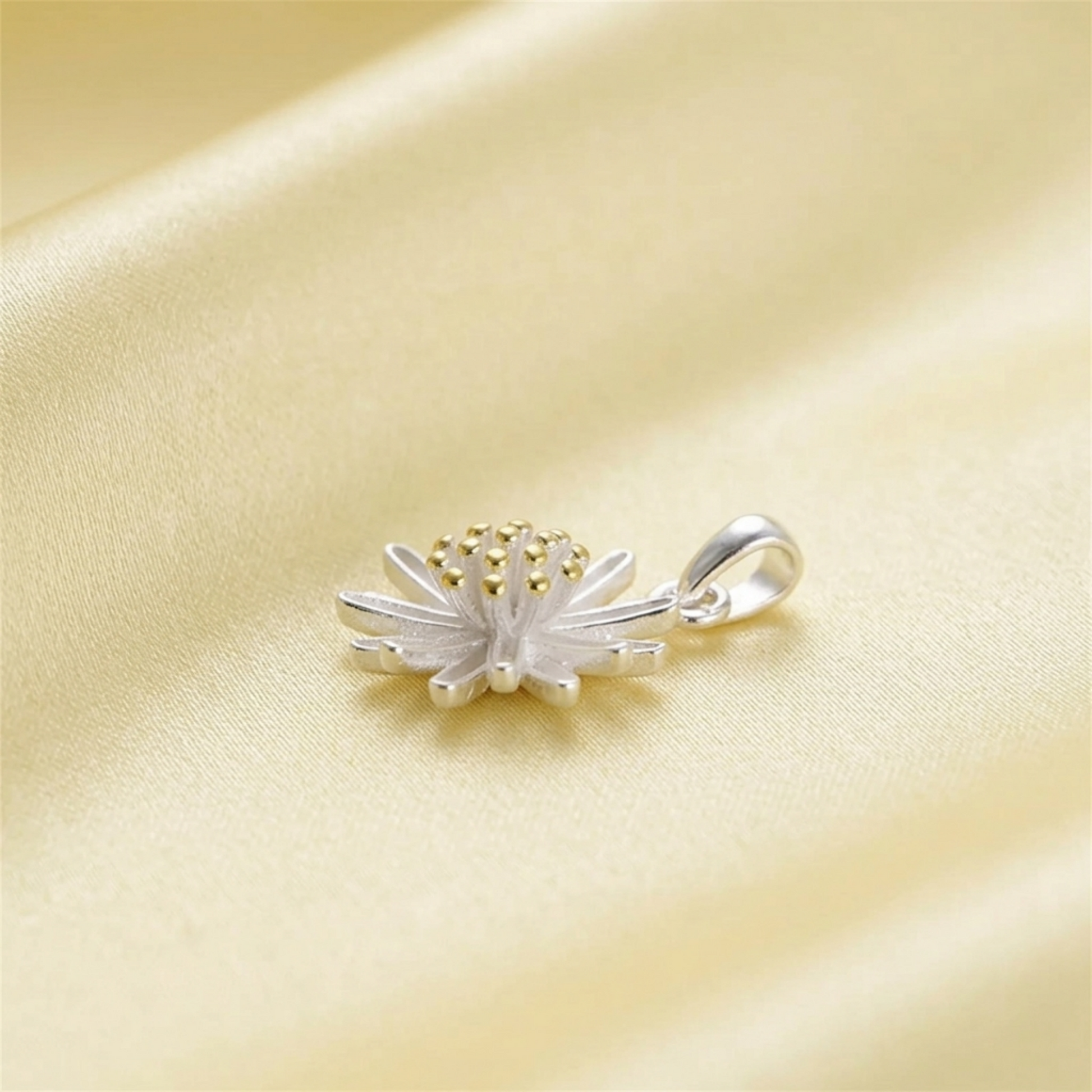 Silver daisy flower pendant with gold center bead, side view on pale fabric