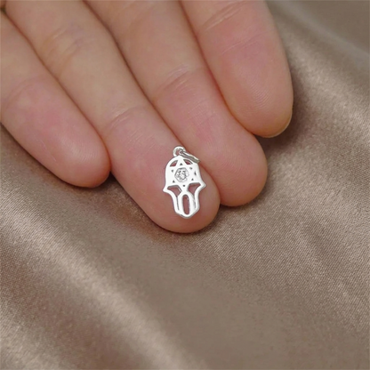 Small silver hamsa protection charm pendant with clear stone on skin