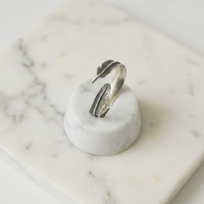 Feather-wing wrap ring in silver with engraved leaf feather motifs, angled view
