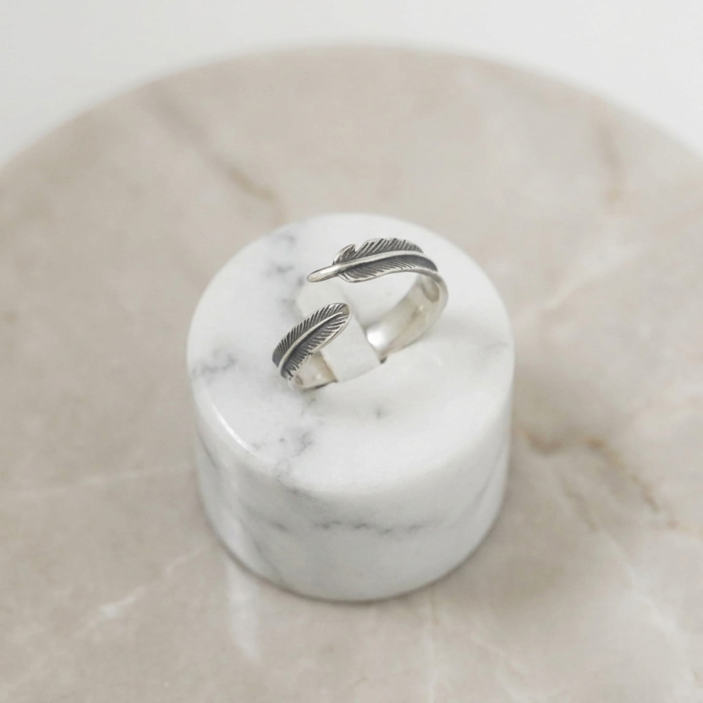 Silver feather wrap ring set on white marble base, two stacked band feathers