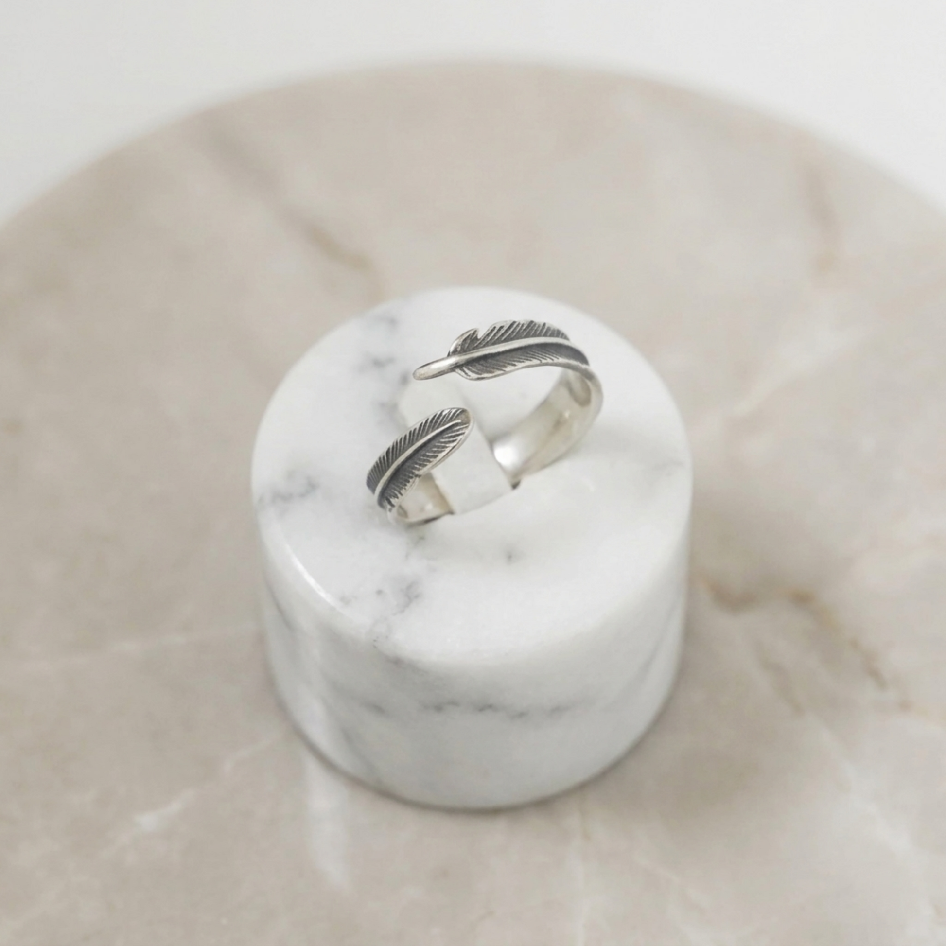 Silver feather wrap ring set on white marble base, two stacked band feathers
