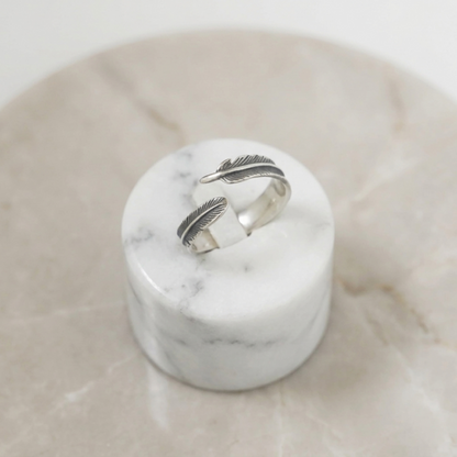 Silver feather wrap ring set on white marble base, two stacked band feathers