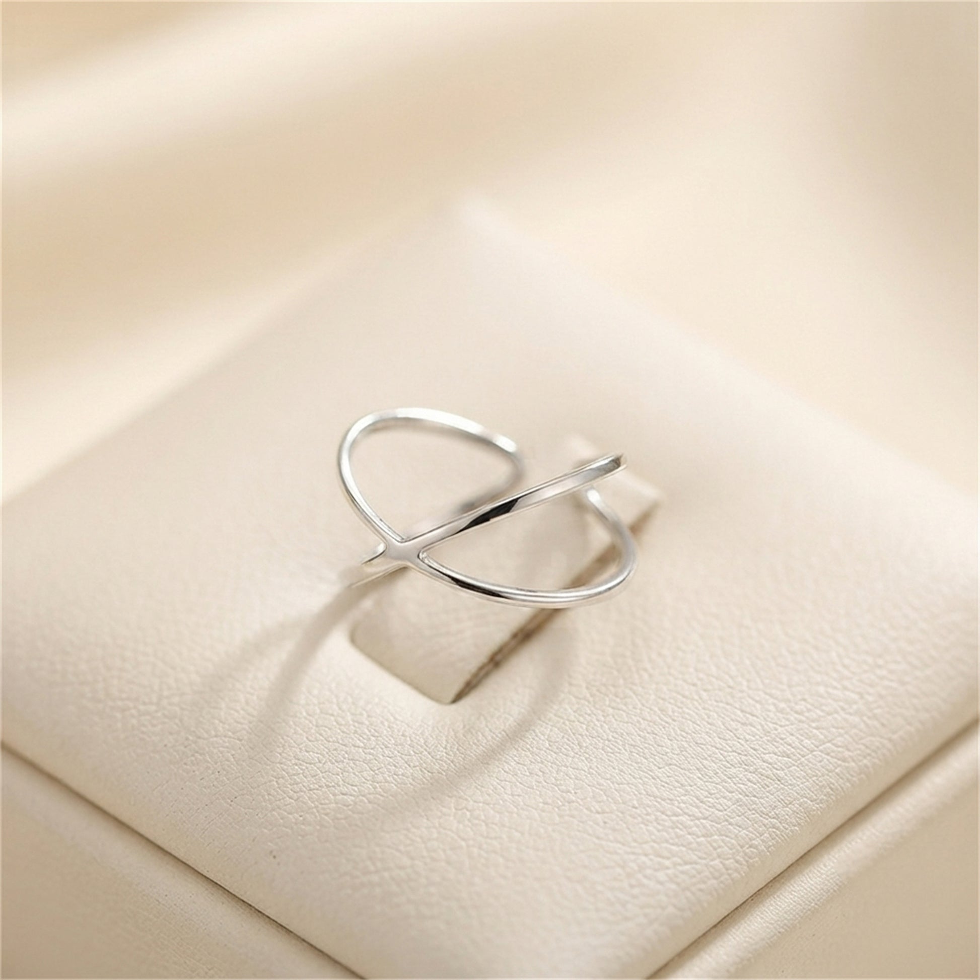 Silver criss-cross love knot ring with crossed bands on a light surface.