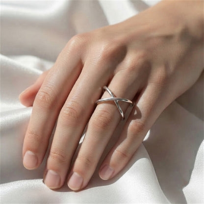 Silver criss-cross love knot ring on finger over white fabric.