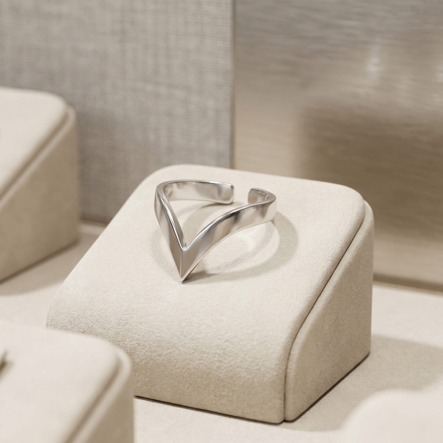Silver wishbone V ring on a beige jewelry box top, polished triangular center.