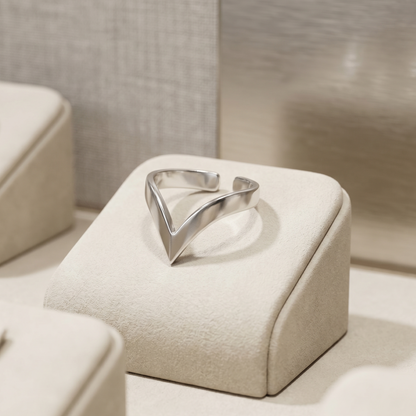 Silver wishbone V ring on a beige jewelry box top, polished triangular center.