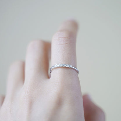 Silver half-eternity beaded ring with clear stones, worn on finger.