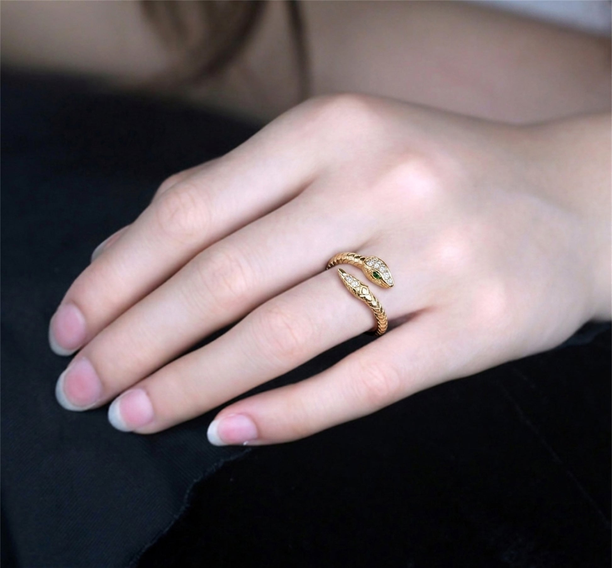 Gold-tone snake wrap ring on hand with green eye and clear stones