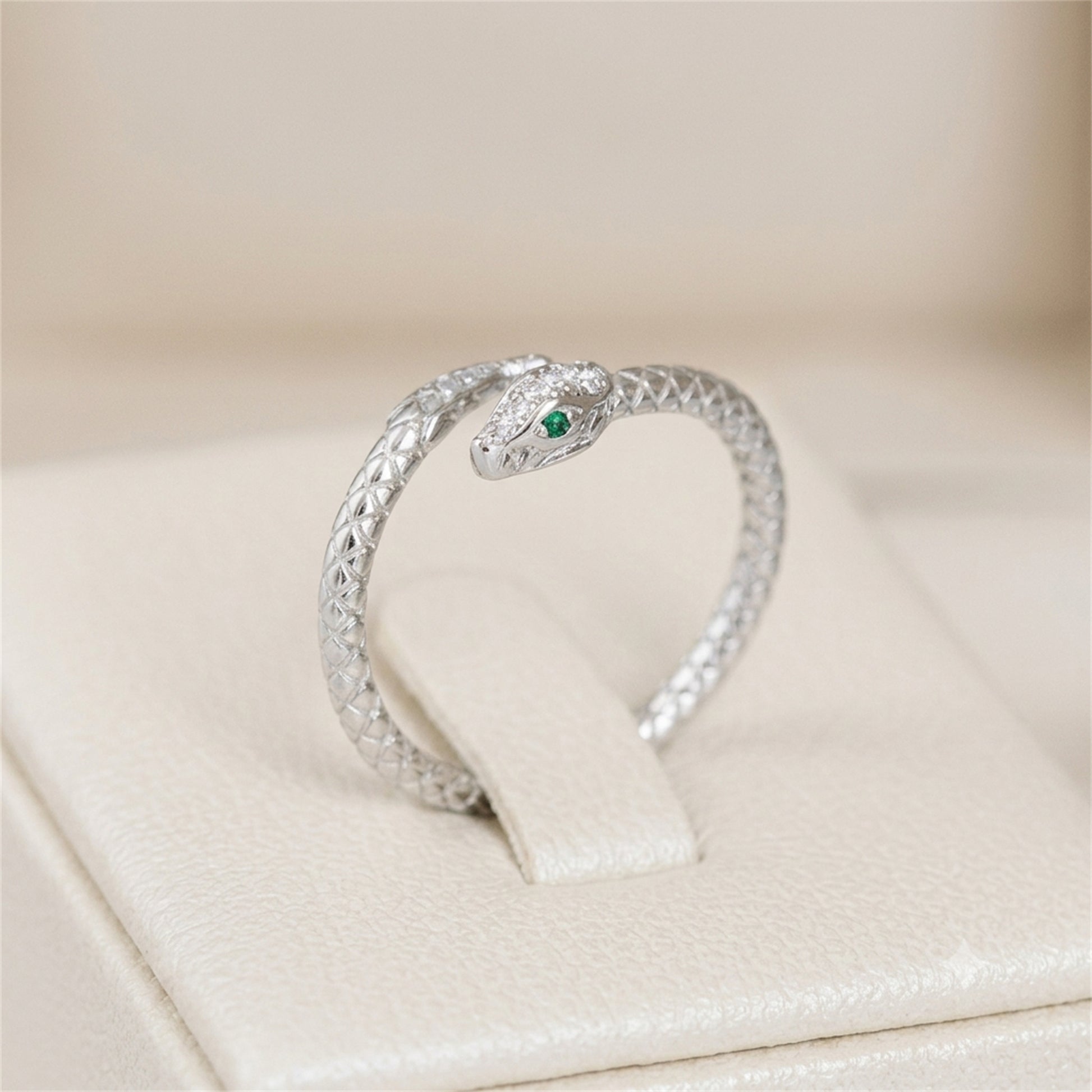 Silver-tone snake wrap ring with green eye and clear stone details
