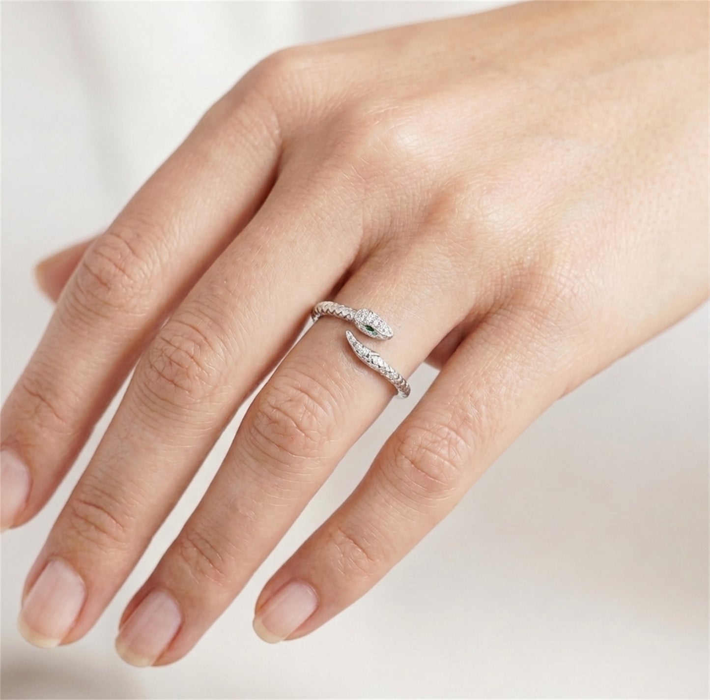 Silver-tone snake wrap ring on hand with green eye and clear stones