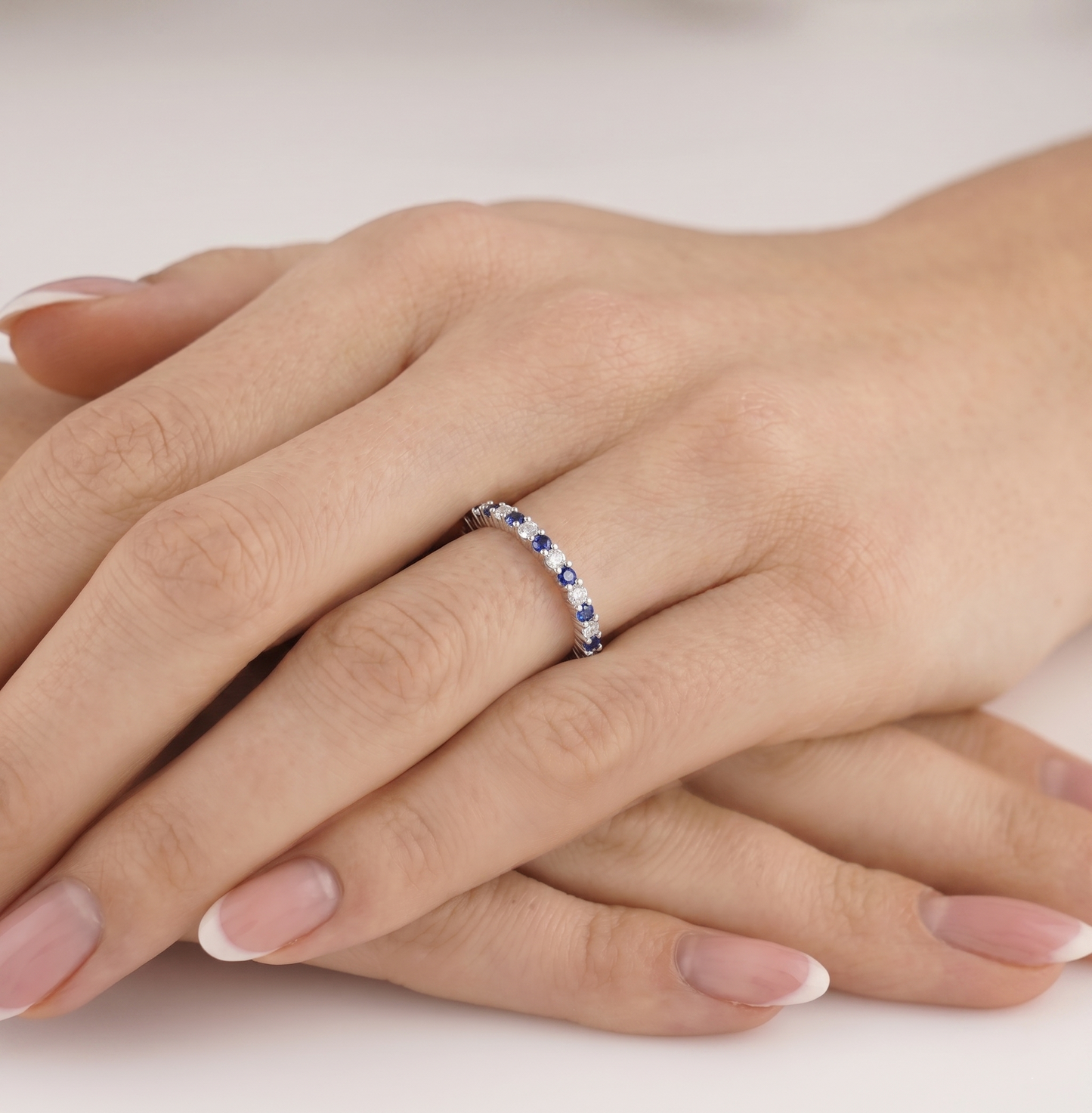 Sapphire Eternity Band on hand, slim silver band with blue stones along the top