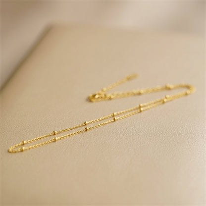 Gold beaded satellite chain necklace close-up, delicate flat links with bead accents.