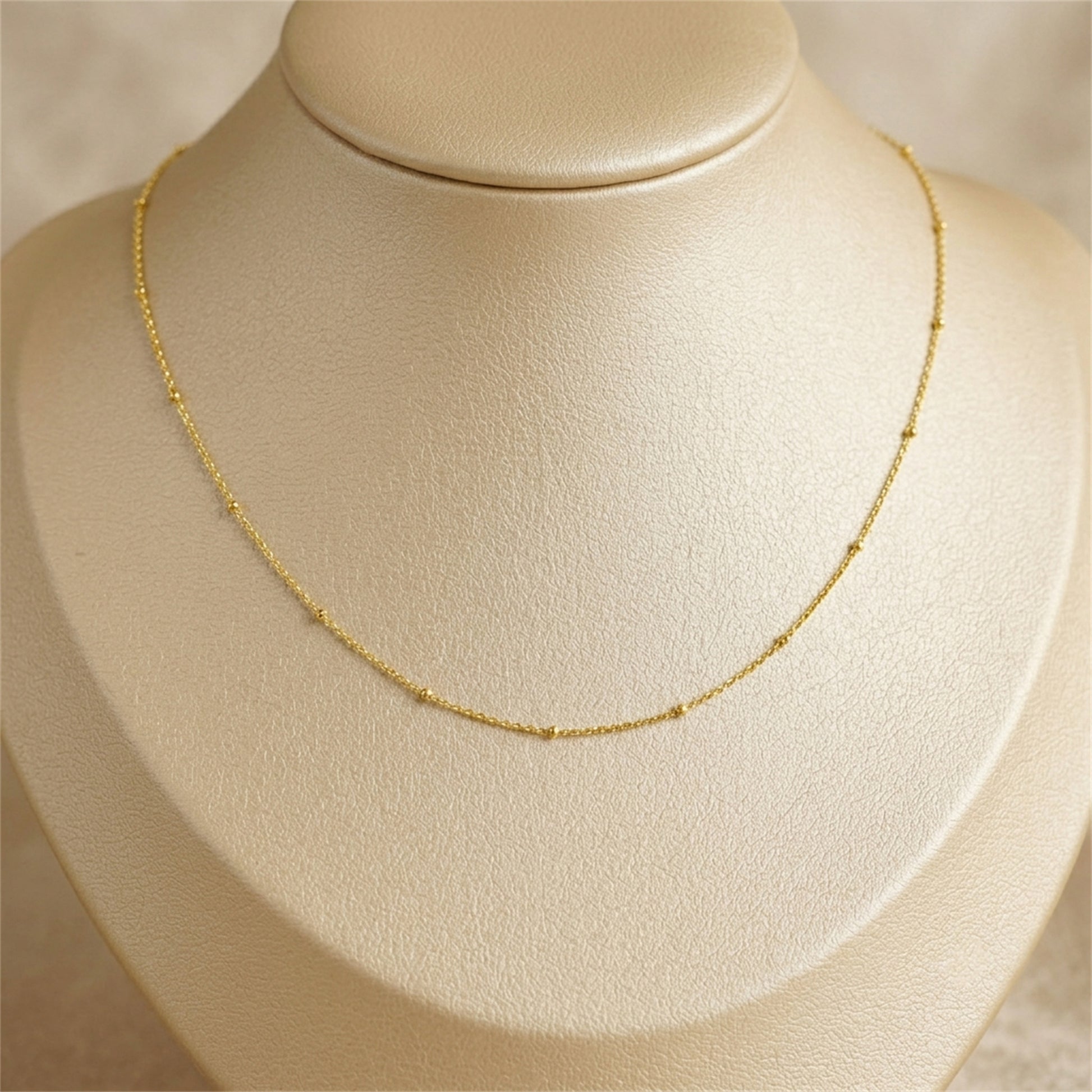 Gold beaded satellite chain necklace on bust, gently curved flat links with beads.