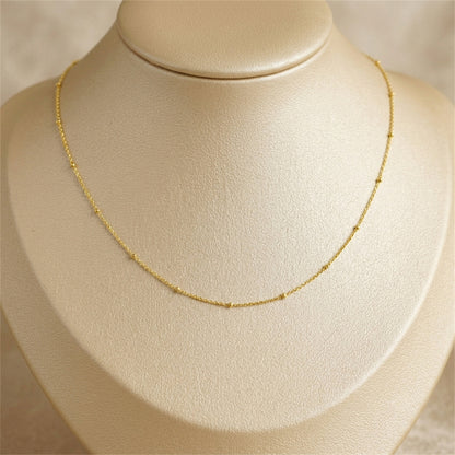 Gold beaded satellite chain necklace on bust, gently curved flat links with beads.