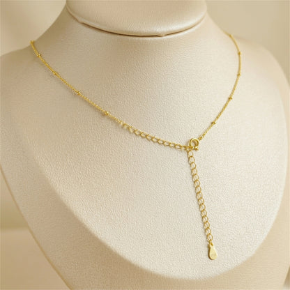 Gold beaded satellite chain necklace with round clasp and dangling drop.