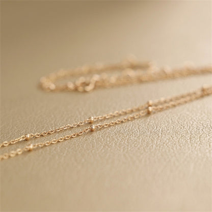Gold beaded satellite chain necklace close-up, tiny round beads along flat links.