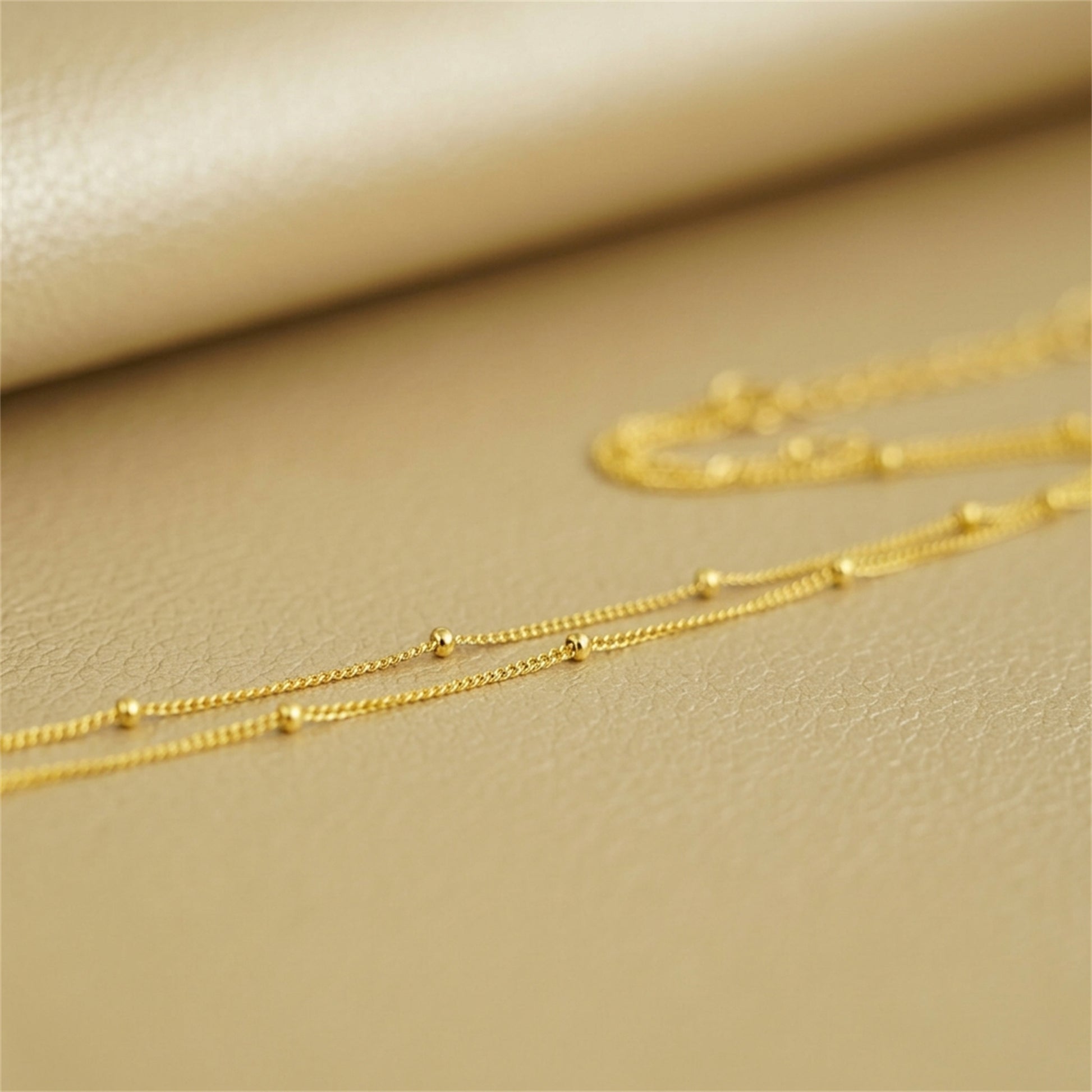 Gold beaded satellite chain necklace, small round bead links in a flat line.