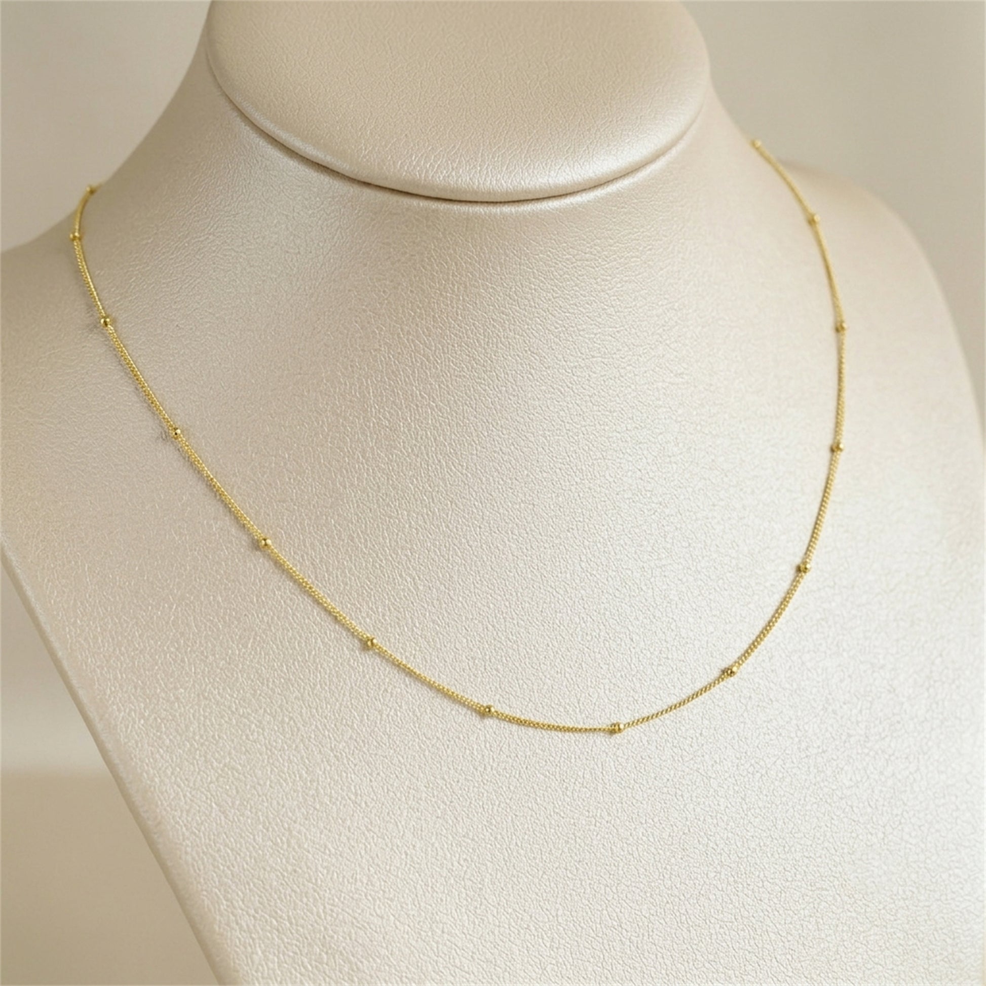 Gold beaded satellite chain necklace on display, smooth link curve with small beads.