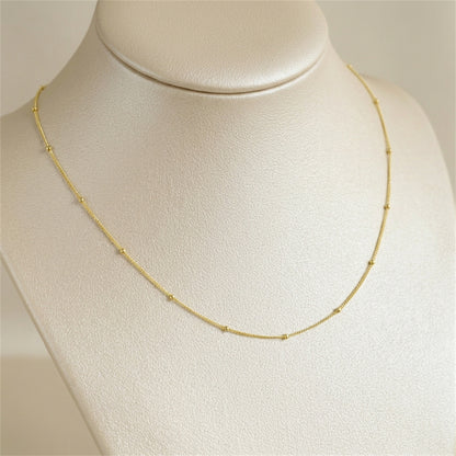 Gold beaded satellite chain necklace on display, smooth link curve with small beads.