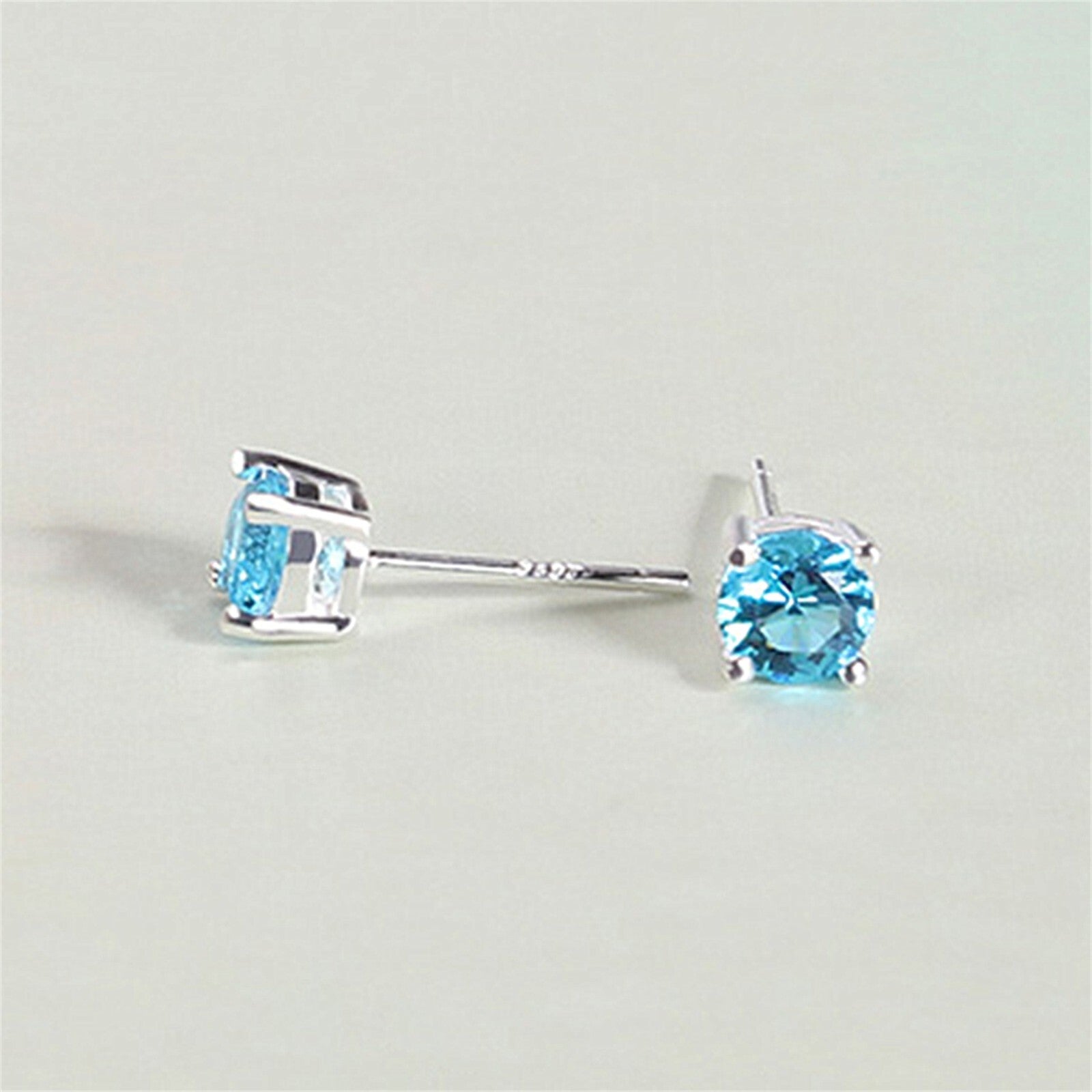 Round CZ solitaire stud earrings showing light blue round stones in prong-set frames
