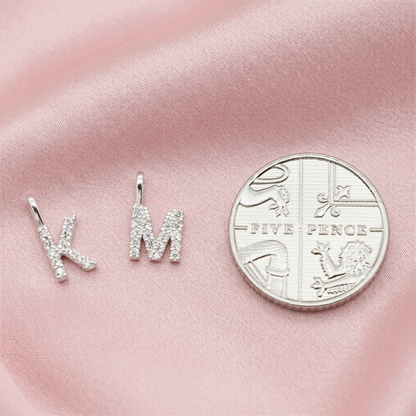 Two rhinestone mini alphabet letter charms next to a coin for size reference