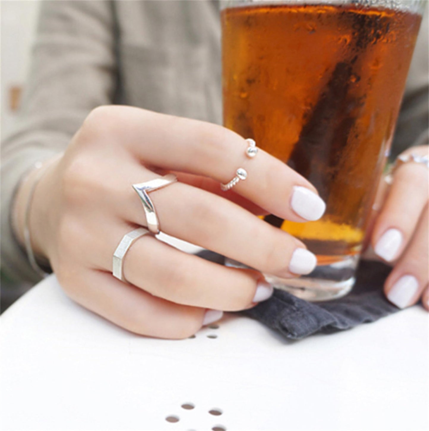 Silver wishbone V ring on a hand near a glass, visible open V profile.